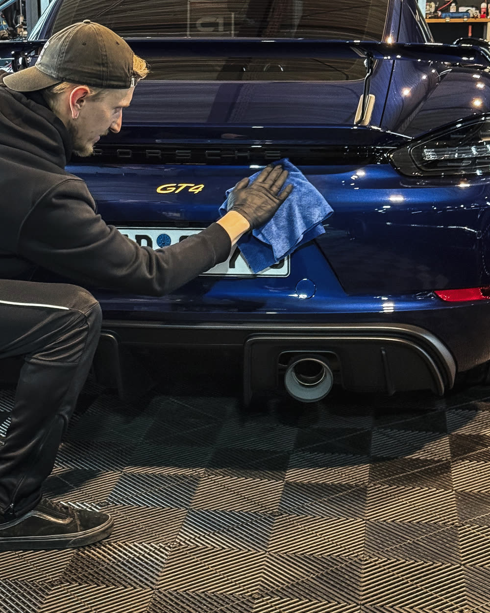 Mitarbeiter poliert das Heck eines Porsche Cayman GT4